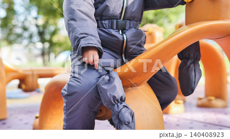 Young child wearing winter overalls playing on a bright playground toy outdoors 140408923
