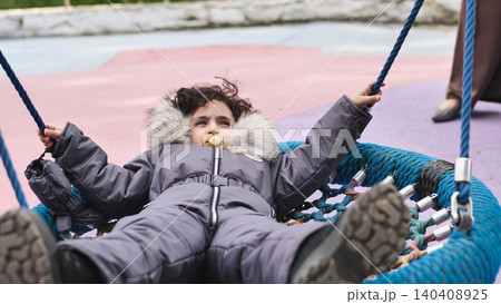 Young child enjoying playground swing in winter snowsuit, embracing childhood fun 140408925