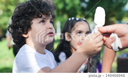 Young boy eagerly watching an adult unwrapping a popsicle for him outdoors 140408948