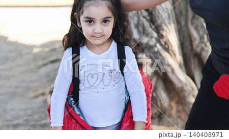 Little girl child looking at camera wearing red jacket outdoors 140408971