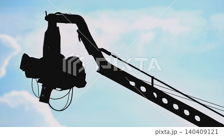 Professional cinema camera on a crane arm, silhouetted against a pale blue sky 140409121