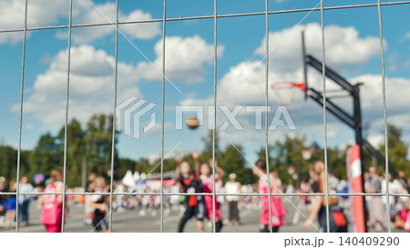 View through a metal fence of a blurred basketball game on a sunny outdoor court. View through a metal fence of a blurred basketball game on a sunny outdoor court. 140409290