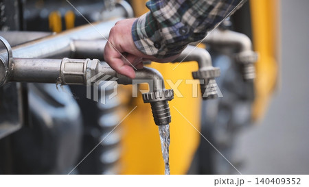 Worker turning industrial metal tap to release flowing water from utility pipeline system 140409352