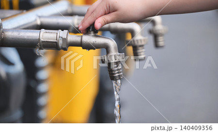 Child hand turning water faucet, saving natural resource and promoting sustainability 140409356