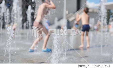 Children running and playing in a city fountain splashing water on a hot summer day Children running and playing in a city fountain splashing water on a hot summer day 140409391