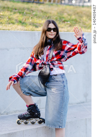 Stylish teenager waving while posing with inline skates in an urban setting 140409487