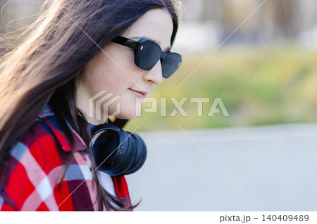 Young stylish woman wearing sunglasses and headphones enjoying music outdoors Young stylish woman wearing sunglasses and headphones enjoying music outdoors 140409489