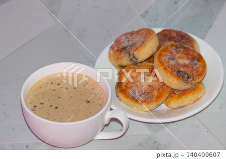Close up of coffee cup foam with blurred cottage cheese pancakes on a plate Close up of coffee cup foam with blurred cottage cheese pancakes on a plate 140409607