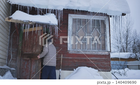 Man entering rustic wooden cabin during cold winter with snow and icicles hanging Man entering rustic wooden cabin during cold winter with snow and icicles hanging 140409690