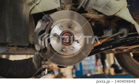 Mechanic performing brake disc and caliper repair on lifted car in Moscow 140409848