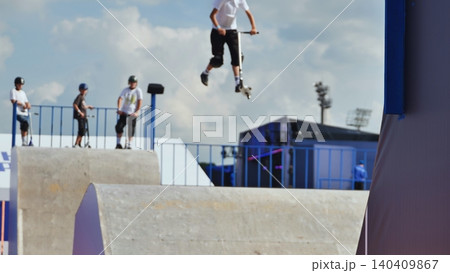 Young boys standing with scooters on a concrete skate ramp at a outdoor park 140409867