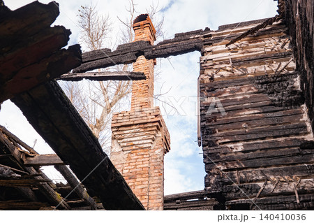 Burnt house remains with charred wood, brick chimney, and open sky after fire Burnt house remains with charred wood, brick chimney, and open sky after fire 140410036