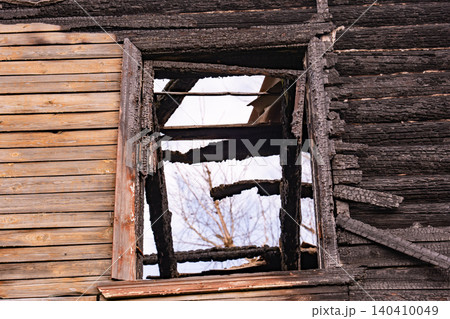 Charred wooden house exterior with a damaged window frame and a partially intact wall 140410049