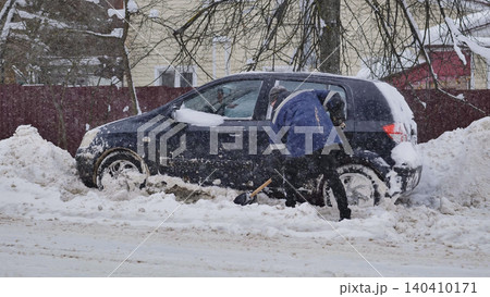 Man shoveling snow around a stuck car during a severe winter blizzard Man shoveling snow around a stuck car during a severe winter blizzard 140410171