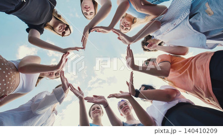 Group of school friends joining hands forming a star shape, symbolizing unity, teamwork, and friendship, against a bright blue sky Group of school friends joining hands forming a star shape, symbolizing unity, teamwork, and friendship, against a bright blue sky 140410209