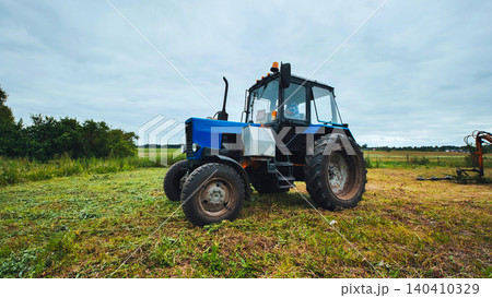 Blue tractor parking in harvested field after mowing grass Blue tractor parking in harvested field after mowing grass 140410329