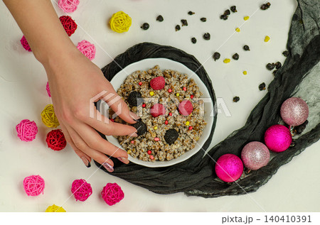Contemporary kutia preparation with woman's hands, white bowl, blackberries, raspberries, colorful candy pearls, and festive decorations on white background. Contemporary kutia preparation with woman's hands, white bowl, blackberries, raspberries, colorful candy pearls, and festive decorations on white background. 140410391