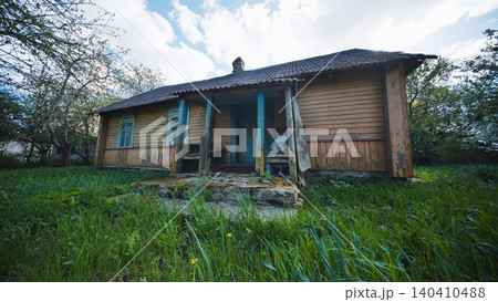 Abandoned old wooden house with porch on overgrown green grass in rural scene Abandoned old wooden house with porch on overgrown green grass in rural scene 140410488