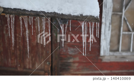 Icicles hanging from a weathered roof ledge over red barn wall Icicles hanging from a weathered roof ledge over red barn wall 140410869