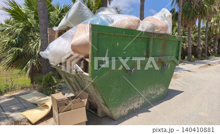 Overflowing construction waste container filled with furniture foam, plastic and cardboard outdoors. Waste management, recycling, renovation cleanup and environmental pollution concept. 140410881