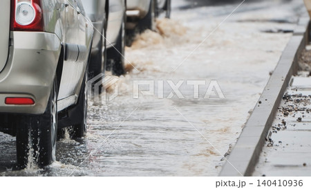 Driving through urban street floods, cars splashing dirty water on a rainy day 140410936