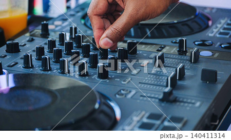 Hand adjusting controls on a DJ mixer controller, creating electronic music at a festival Hand adjusting controls on a DJ mixer controller, creating electronic music at a festival 140411314