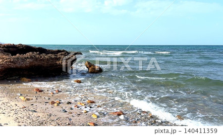 Rocky shoreline with gentle waves under a pale blue sky Rocky shoreline with gentle waves under a pale blue sky 140411359