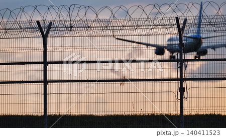 Airport fence with barbed wire and approaching airplane at sunset Airport fence with barbed wire and approaching airplane at sunset 140411523