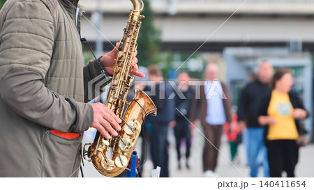 Street musician performing jazz music with a saxophone for passersby on a city sidewalk. Street musician performing jazz music with a saxophone for passersby on a city sidewalk. 140411654