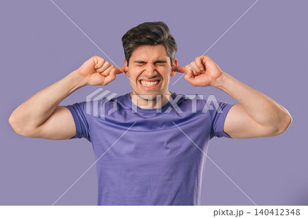 Young man Covering Ears, Showing Irritation In Violet Studio. Stress, Overload Young man Covering Ears, Showing Irritation In Violet Studio. Stress, Overload 140412348