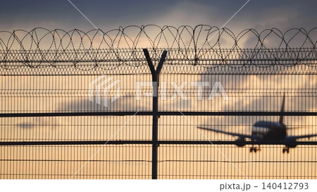 Airport fence with razor wire, an airplane landing in the background at sunset Airport fence with razor wire, an airplane landing in the background at sunset 140412793
