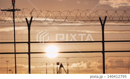Airport security fence with barbed wire at sunset, protecting restricted area Airport security fence with barbed wire at sunset, protecting restricted area 140412795