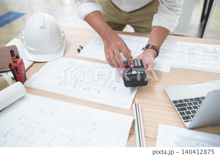 Construction Professional Using Calculator on Architectural Plans for Project Management Construction Professional Using Calculator on Architectural Plans for Project Management 140412875