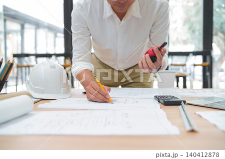 Construction professional reviewing blueprints with measuring tape and calculator Construction professional reviewing blueprints with measuring tape and calculator 140412878