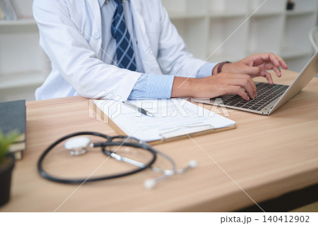 Medical Professional Typing on Laptop While Working with Patient Records and Stethoscope 140412902
