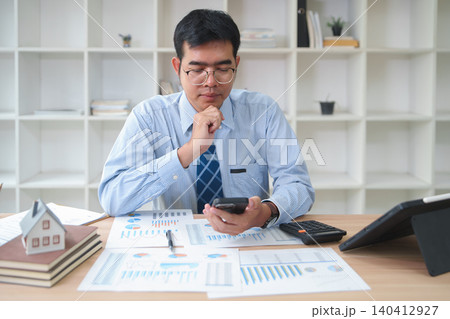 Businessman Analyzing Financial Reports and Data on Smartphone in Office Setting Businessman Analyzing Financial Reports and Data on Smartphone in Office Setting 140412927