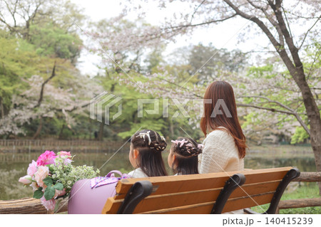桜咲く公園のベンチで過ごす母親と姉妹の春のひととき 140415239