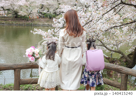 桜咲く公園で春の景色を眺める母親と姉妹の後ろ姿 140415240