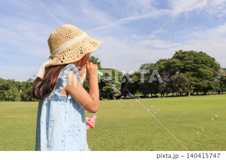 青空の下でシャボン玉遊びを楽しむ麦わら帽子の女の子 140415747