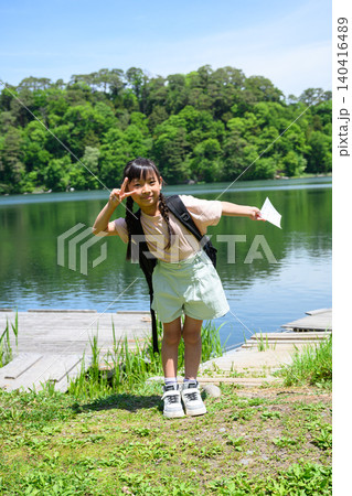 新緑の湖畔でリュックを背負い笑顔でピースサインをする遠足の女子小学生 新緑の湖畔でリュックを背負い笑顔でピースサインをする遠足の女子小学生 140416489