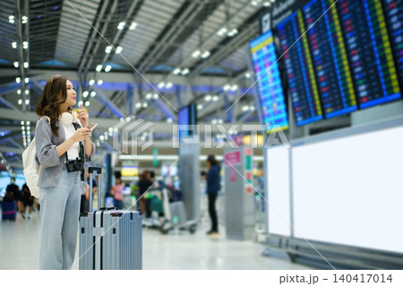 Asian woman holding passport and boarding pass while checking flight schedule. Asian woman holding passport and boarding pass while checking flight schedule. 140417014