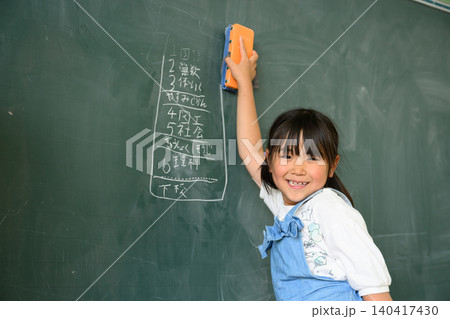教室で笑顔で黒板を消す低学年の女子小学生 教室で笑顔で黒板を消す低学年の女子小学生 140417430