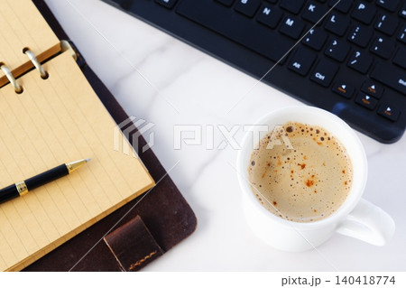 リング式のシステム手帳を広げ、コーヒー（カフェ・ラテ）を飲みながらパソコンでデスクワーク中のイメージ 140418774