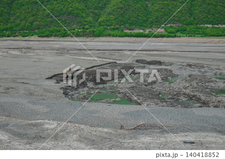 Industrial excavator digging in a dry, cracked earth landscape with green forest background Industrial excavator digging in a dry, cracked earth landscape with green forest background 140418852