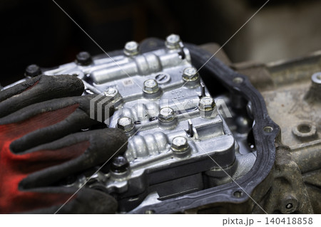 Close up of a textured mechanic glove resting on a complex metal hydraulic gearbox valve body Close up of a textured mechanic glove resting on a complex metal hydraulic gearbox valve body 140418858