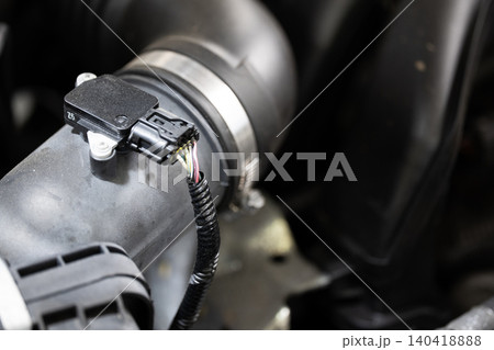 Close-up of a black MAF sensor mounted on a vehicle air intake pipe with wiring harness Close-up of a black MAF sensor mounted on a vehicle air intake pipe with wiring harness 140418888