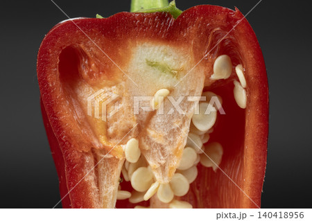 Detailed internal view of a cut red bell pepper showing fresh white seeds and pulp against dark background Detailed internal view of a cut red bell pepper showing fresh white seeds and pulp against dark background 140418956