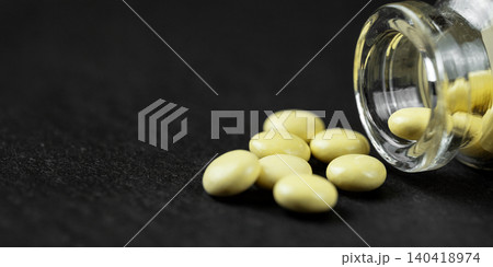 Round yellow medicine tablets spilling out of a small glass vial on a dark surface Round yellow medicine tablets spilling out of a small glass vial on a dark surface 140418974
