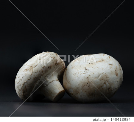 Minimalist composition of two raw champignon mushrooms on a dark surface with moody dramatic lighting 140418984
