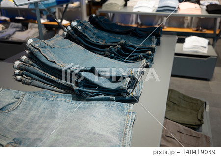 Close-up shot of folded blue denim trousers neatly stacked on a gray display table in a boutique Close-up shot of folded blue denim trousers neatly stacked on a gray display table in a boutique 140419039